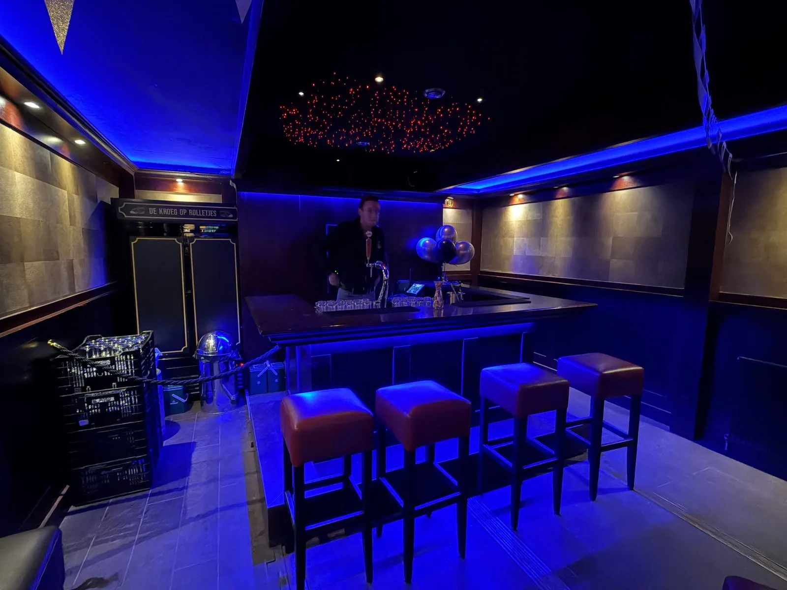 De bar van De Kroeg XL met een barman achter de tap en blauwe sfeerverlichting.