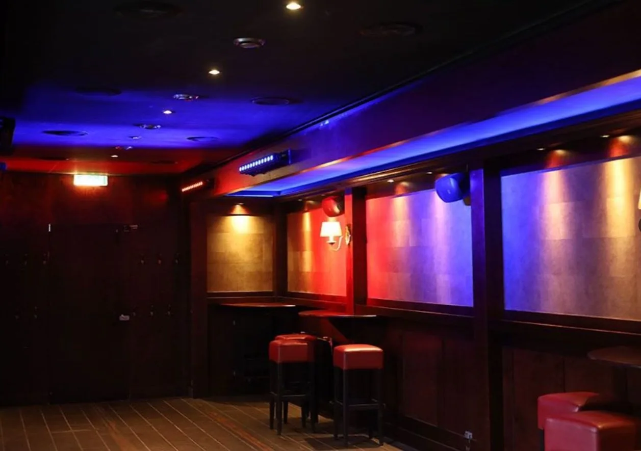 De zithoek in Kroeg XL met houten lambrisering, rode krukken en blauw-rode sfeerverlichting.