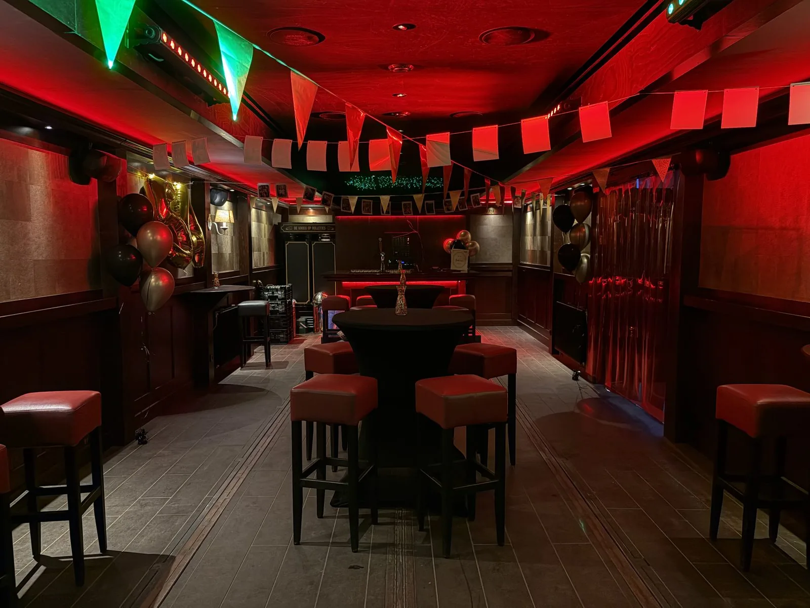 Het interieur van De Kroeg XL in rood licht, met vlaggetjes en ballonnen voor een feest.