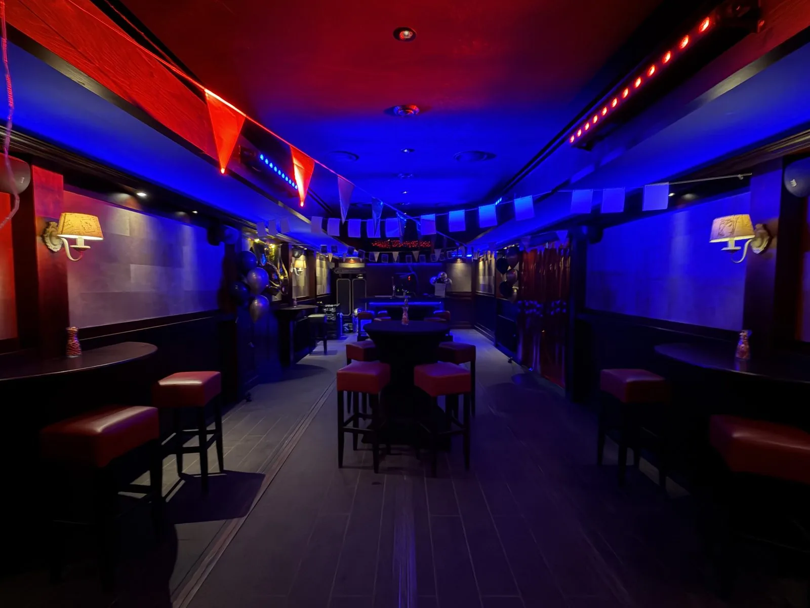 Statafels en krukken in De Kroeg XL onder rood-blauwe verlichting.