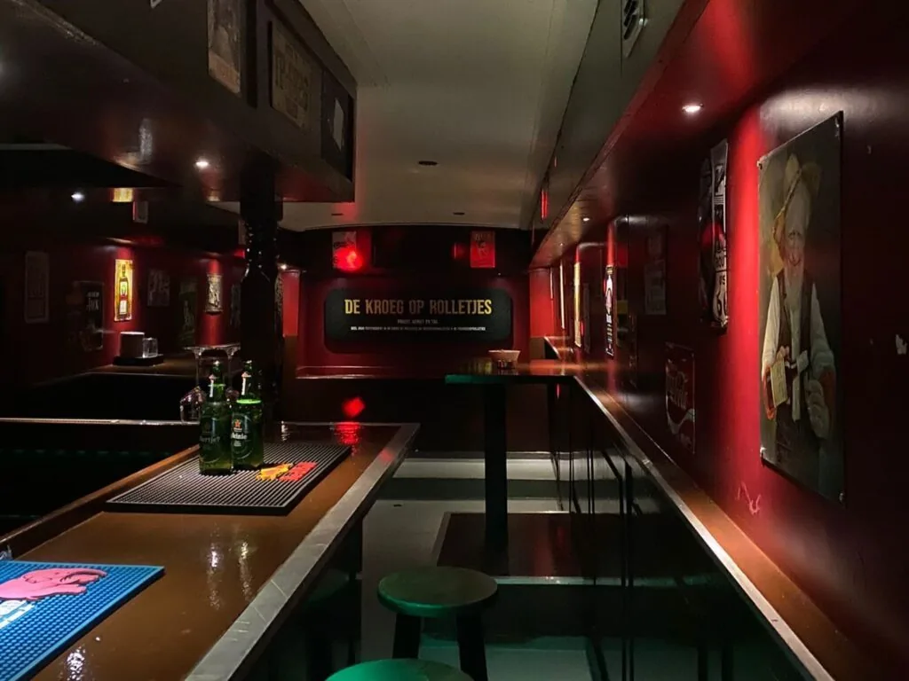 De bar in de Kroegbus met rode wanden en drankjes op de toog.
